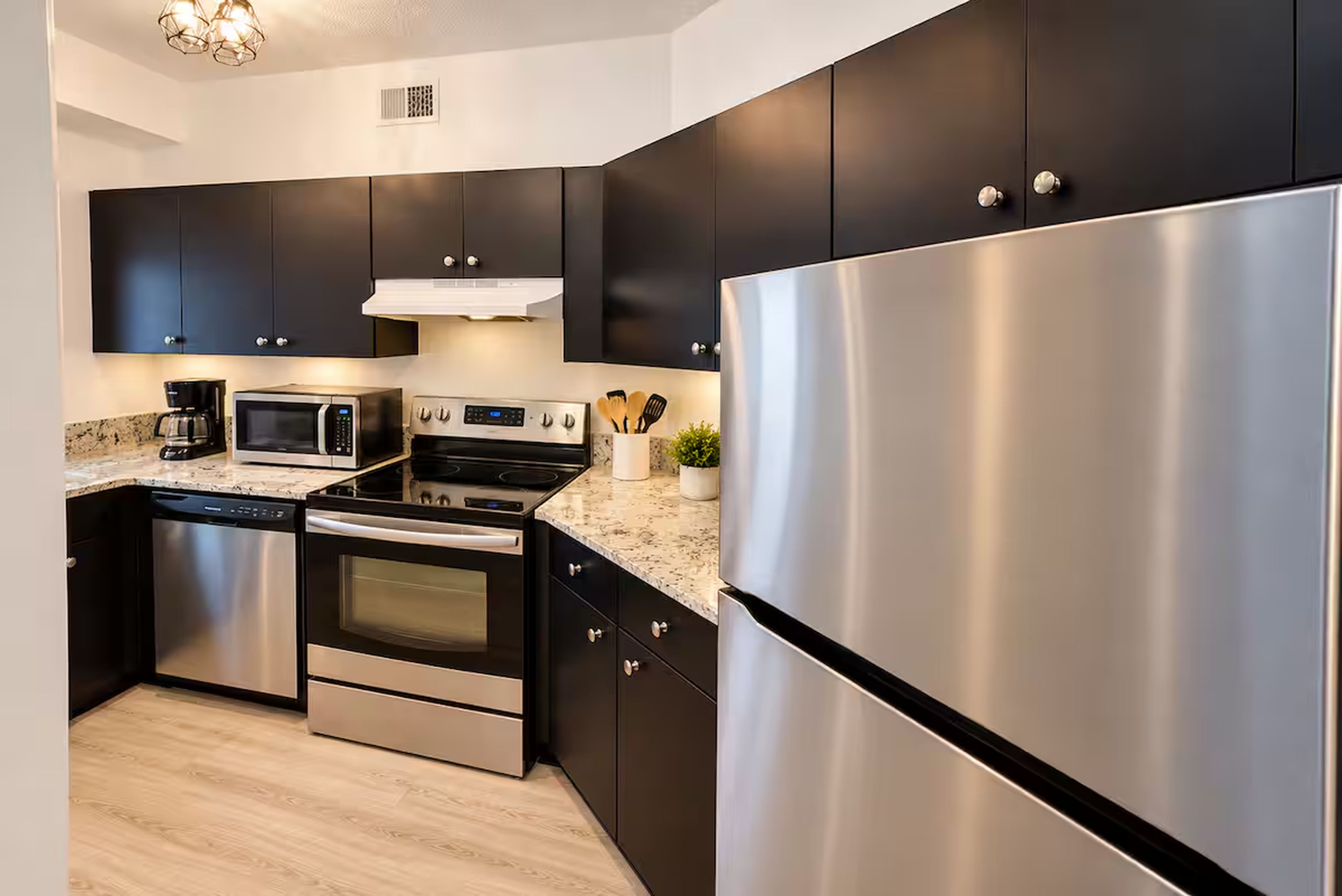 A modern kitchen with stainless steel appliances, dark cabinetry, and a granite countertop.