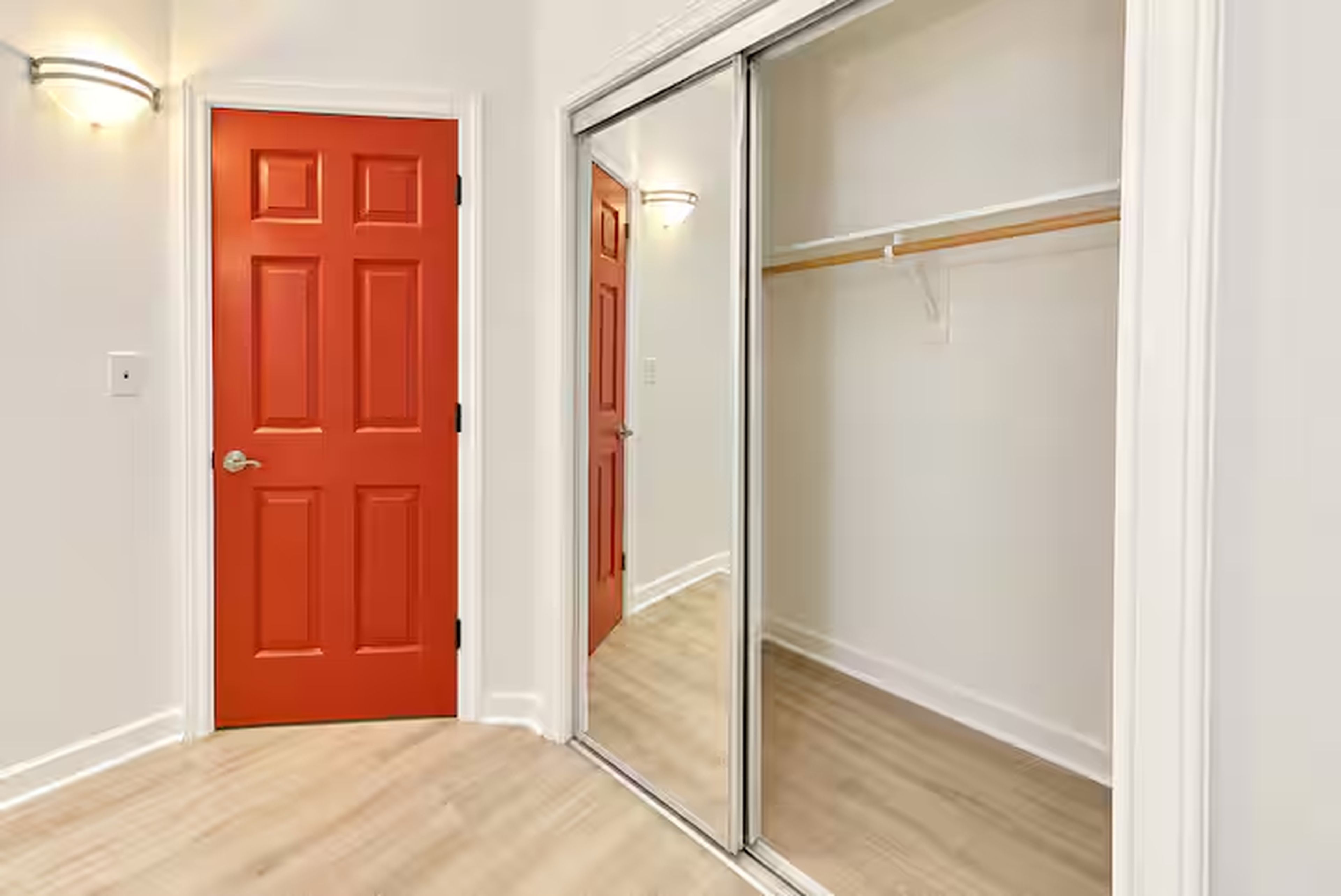 Een kamer met een rode deur, een schuifdeur voor de inloopkast en een lichtschakelaar aan de muur.