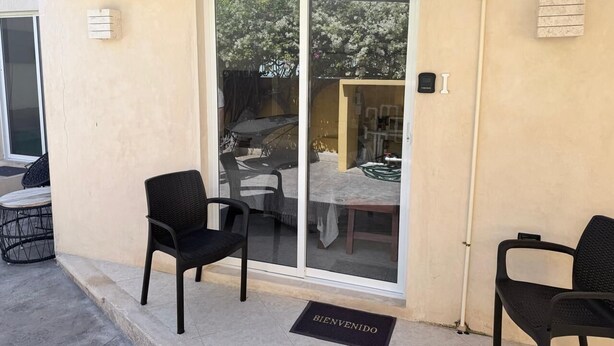 A patio with two black chairs, a table, and a sliding glass door leading to an interior space.