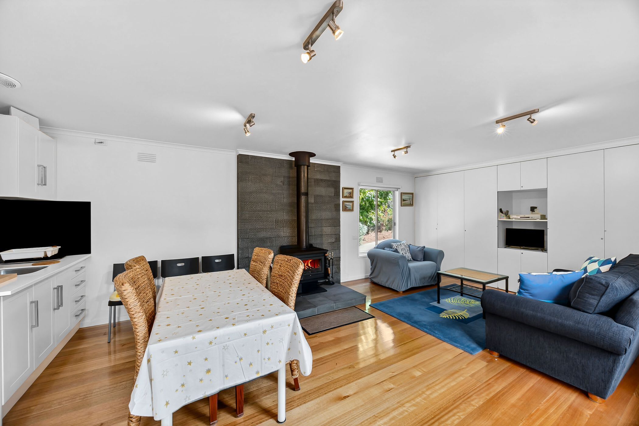 A modern kitchen with white cabinets, a dining table with a star-patterned tablecloth, and a built-in wood stove.
