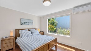 Un dormitorio con cama de madera, una mesita de noche, una lámpara de noche, una ventana con vistas a zonas verdes y una lámpara en el techo.