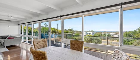 A spacious room with a large dining table, wicker chairs, and a view of the outdoors through large windows.