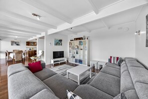Ein modernes Wohnzimmer mit grauen Sofas, einem weißen Couchtisch, einem Fernseher und einem Bücherregal.