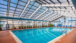 Une piscine intérieure dotée d’un toit en verre, de plantes en pot et de chaises longues bleues.