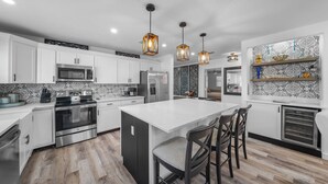 A modern kitchen with white cabinets, stainless steel appliances, and a central island with bar stools. - New! Gulf Breeze - Stunning Heated Saltwater Pool & Spa with Sundeck, Apprx 1 Mile to Beach! (Naples)