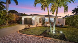 A residential house with a garage, a well-maintained lawn, and palm trees. - New! Gulf Breeze - Stunning Heated Saltwater Pool & Spa with Sundeck, Apprx 1 Mile to Beach! (Naples)