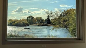 Kehyksiin asetettu maisemamaalaus, jossa on kuvattuna joki, puita ja kirkas taivas.