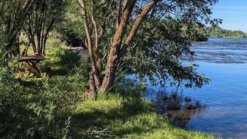 A riverside picnic area with a bench and picnic table, surrounded by trees and grass.