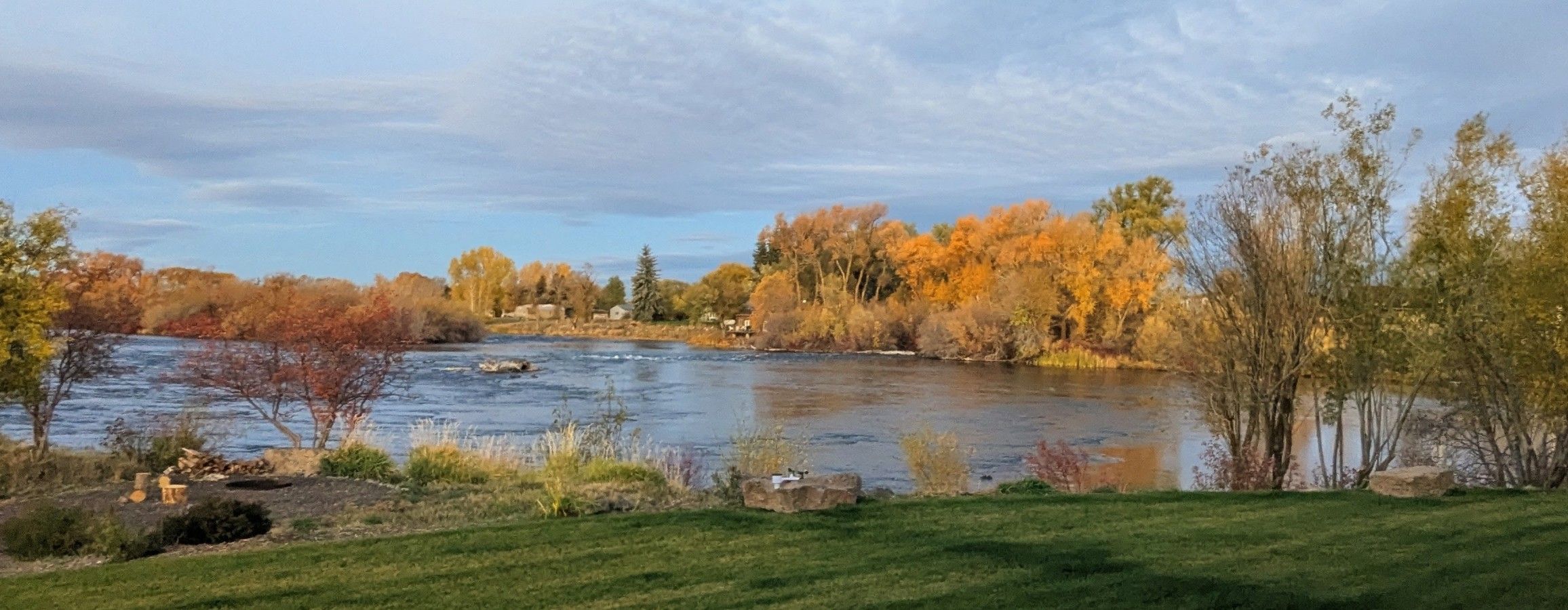 A river with autumn foliage, a grassy foreground, and a clear sky.
