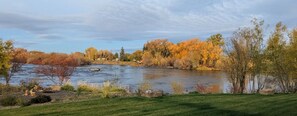 A river with autumn foliage, a grassy foreground, and a clear sky.