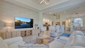 Una sala moderna con un televisor de pantalla plana grande, un sofá cómodo, una mesa de centro y una cocina al fondo.