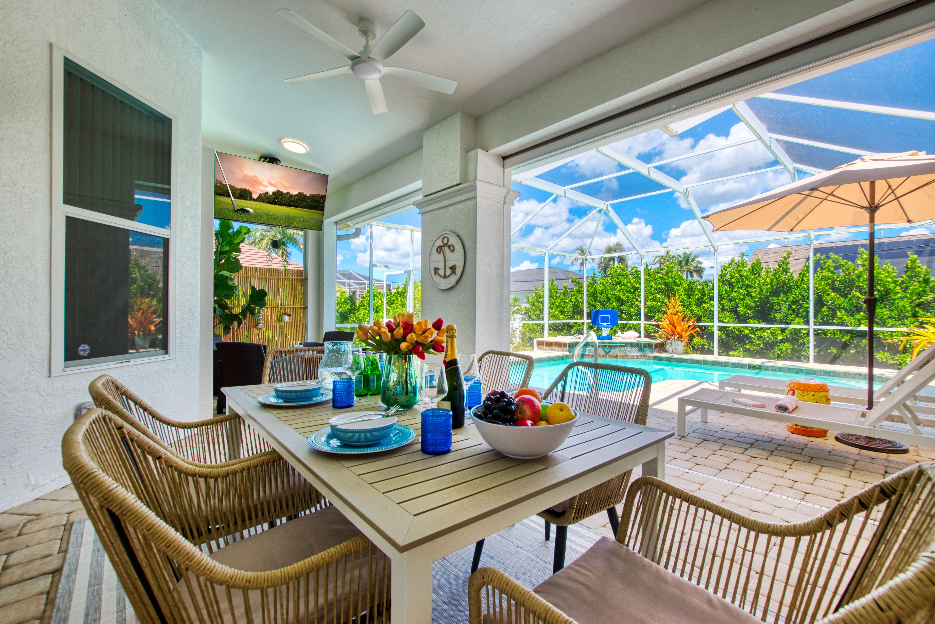 A dining area with a table set for four, surrounded by wicker chairs, a ceiling fan, and a view of a swimming pool.
