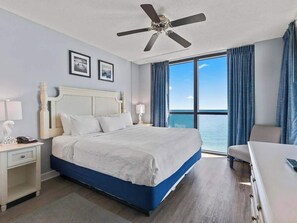 Ein Hotelzimmer mit Bett, Schreibtisch, Stuhl, Deckenventilator und einem großen Fenster mit Vorhängen.