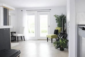 Ein modernes Wohnzimmer mit einer weißen Tür, einem schwarzen Sofa, einem grünen Ottomanen und einer Topfpflanze.