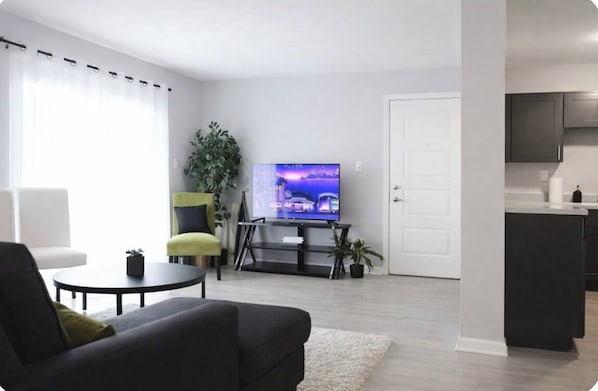 Ein modernes Wohnzimmer mit Flachbildfernseher, einer Couch, einem Couchtisch und einer kleinen Pflanze.