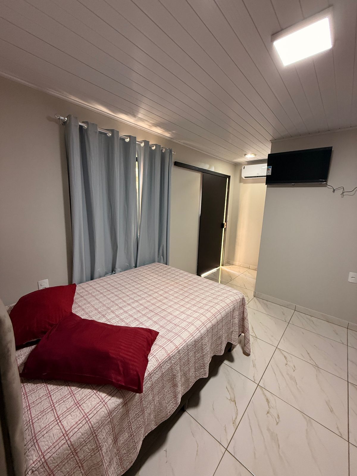 Quarto com cama, cortinas, televisão de tela plana e ar condicionado.