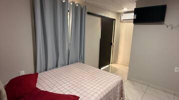 Quarto com cama, cortinas, televisão de tela plana e ar condicionado.