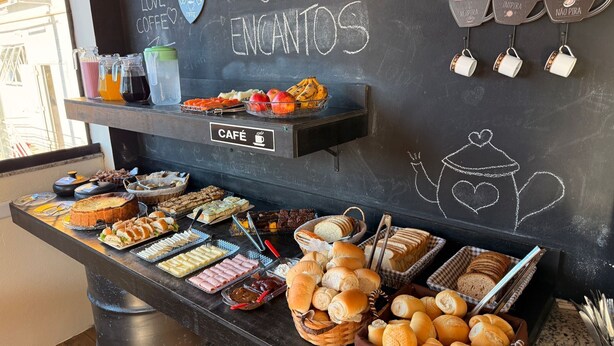 A café counter with a variety of pastries, sandwiches, and drinks. - POUSADA MARÉ DE ENCANTOS (Penha)