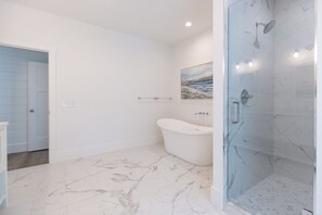 A bathroom with a glass-enclosed shower, a freestanding bathtub, and a door leading to another room. - Grand Opening June 13! New 6BR/5.5 Bath Luxury - Sleeps 18 - 4 rows to the Beach (Hilton Head Island)