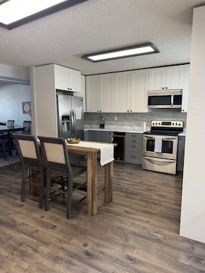 Una cocina moderna con armarios blancos, electrodomésticos de acero inoxidable y una mesa de comedor de madera.