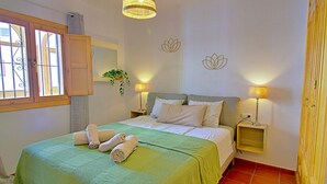 Una camera da letto con un letto, due lampade sui comodini, una finestra con sbarre, uno specchio e un elemento decorativo al muro.