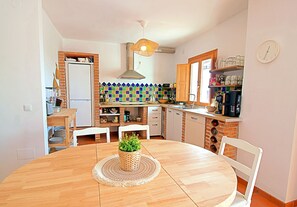 A kitchen with a round wooden table, white chairs, a hanging light fixture, and a clock on the wall. - Costa Del Sol apartment in the village of Frigiliana (Frigiliana)