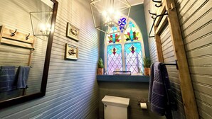 Ein Badezimmer mit einem großen Spiegel, Holzvertäfelung, einer weißen Toilette und einem farbigen Glasfenster.