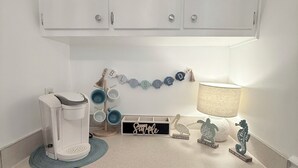 Una cocina con armarios blancos, una cafetera, una bandeja de recipientes, un letrero con 'Paradise Found' y elementos decorativos como un caballito de mar y una tortuga.