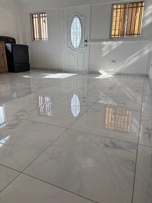 A spacious room with a glossy tiled floor, a white door with a decorative glass panel, and barred windows.