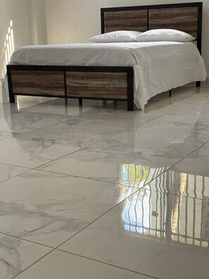A bed with a wooden frame and white bedding in a room with a shiny tiled floor.