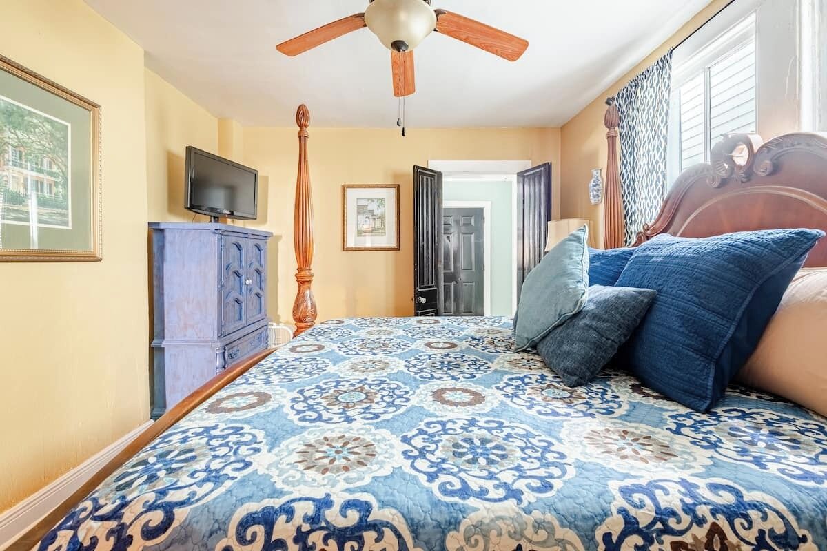 Une chambre à coucher avec une couvre-lit à motifs, un ventilateur de plafond, un téléviseur et une armoire en bois.