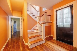 Eine Treppe führt zu einer oberen Etage, eine schwarze Tür mit Fenster und ein Flur mit Holzdielen.