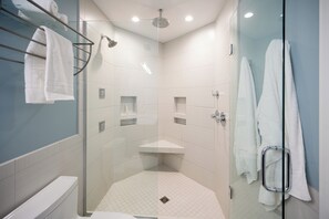 A modern bathroom with a glass-enclosed shower, white tiles, and a glass partition.