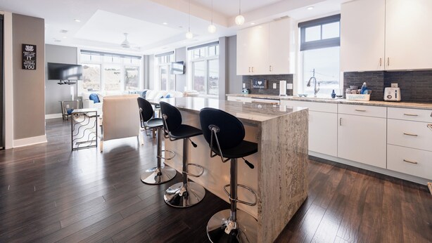 Een moderne keuken met witte kastjes, een marmeren eiland en een bar met zwarte barkrukken.