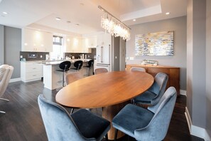 Une cuisine moderne avec des meubles blancs, un îlot central doté de tabourets et un lustre.