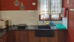 Une cuisine avec des meubles de rangement en bois, un plan de travail noir, un évier, une fenêtre avec des rideaux légers et un four à micro-ondes placé à gauche.