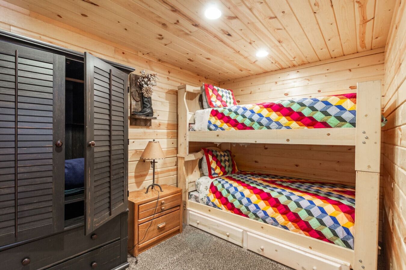 Una habitación de cabaña de madera con literas, un pequeño armario de madera y una lámpara.
