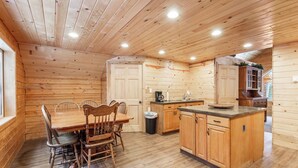 Ein Holzblockhaus-Innenraum mit Esstisch, Stühlen, einer Küchenzeile und einer kleinen Kochinsel.