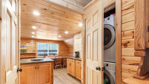 Ein Blockhaus-Interieur mit Holzwänden, einer Küchenzeile, einem Esstisch mit Stühlen und einer Waschmaschine.