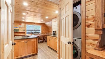 Een houten interieur met een keukenhoek, een eettafel met stoelen en een wasmachine.