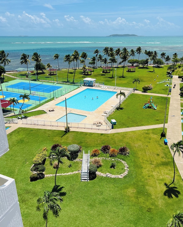 Une piscine avec un toboggan, entourée de palmiers et offrant une vue sur l’océan.