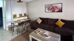 Una sala de estar moderna con un sofá marrón, una mesa de centro de madera y un comedor con una mesa y sillas blancas.