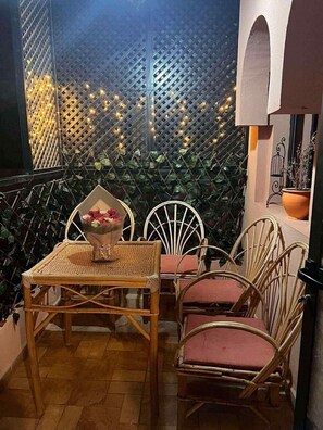 Ein gemütlicher Sitzbereich im Freien mit Korbstühlen und einem Tisch, umgeben von einer Spalierwand mit Lichterketten.