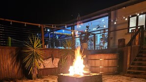 An outdoor patio with a fire feature, wooden seating, and a view of the building's interior.