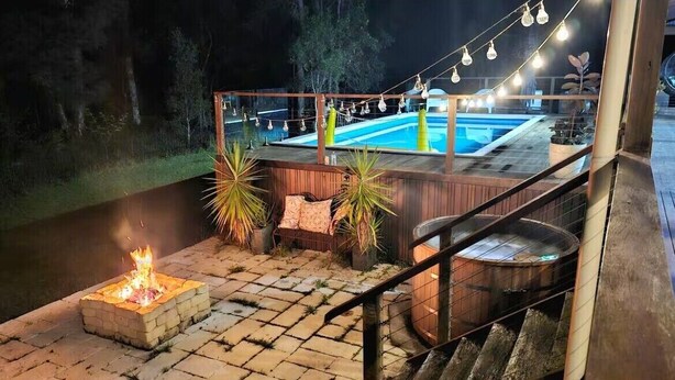A poolside area with a fire pit, outdoor seating, and string lights.