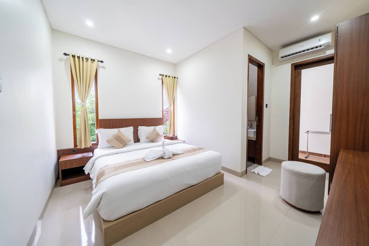 A modern hotel room with a large bed, wooden headboard, and a small seating area.