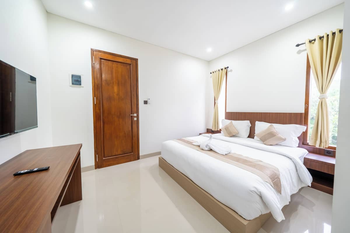 A hotel room with a bed, a wooden desk, a television, and a window with curtains.