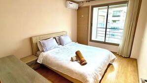 Ein Hotelzimmer mit einem Bett, einem Nachttisch aus Holz, einem Fenster mit Vorhängen und einer Klimaanlage an der Wand.