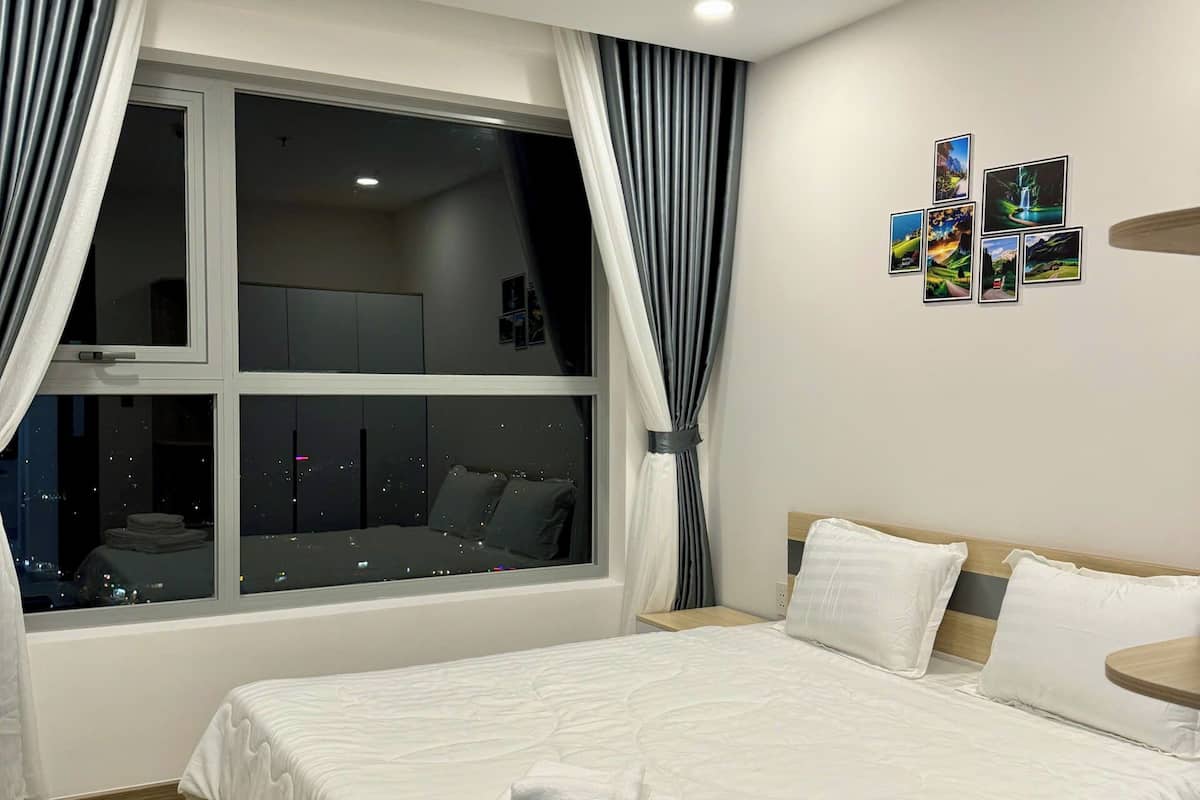 Een moderne hotelkamer met een groot bed, een houten hoofdbord, een nachtkastje en een raam met gordijnen.
