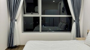 Habitación de hotel con una cama grande, una ventana con cortinas y vistas a la ciudad de noche.